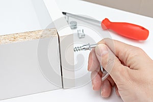 Close up view of a person assembling new white drawer using a screwdriver, tighten a screw with a hex allen key