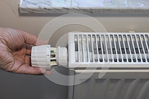 Close up view of person`s hand turning off thermostat on heating radiator to save energy.