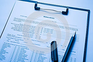 Close up view photo of patient medical history blank form on clipboard with black pen lying on doctors desk