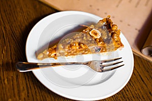The close-up view of the piece of the honey cake covered with bananas and nuts.