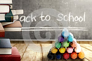 Close up view of pile of books and colorful crayons on wooden table and blackboard with Back to School message