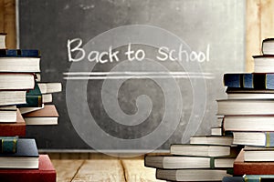 Close up view of pile of books on wooden table and blackboard with Back to School message