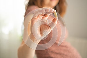 Close-up view of pill in hand. In the background is pregnant woman. Taking vitamins during pregnancy