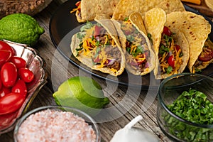 Close-up view of plate with hot mexican tacos on rustic wooden table with ingredients for cooking background. Concept of