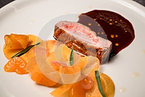 Close-up view of plate with piece of meat with sauce and slices of mandarin.