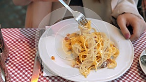 Close-up view of plate with spaghetti. Young happy woman sitting in cafe ang eating pasta after long busy day.