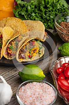 Close-up view of plate with tasty mexican tacos on rustic wooden table with ingredients for cooking background. Concept of
