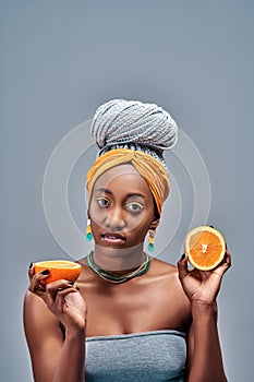 Close up view portrait of a beautiful young afro american woman with bright color make-up holding half of an orange near the face