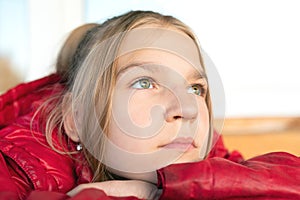 Close up view portrait of young blonde green-eyed girl. She put her chin on arm looking upwards wistfully and pensively full of