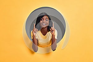 Close-up view portrait of young cheerful woman pointing two fingers up isolated in a round hole in bright yellow background. Copy