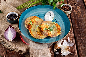 Close-up view of potato pancakes. Potato cake on a blue plate above a wooden table, with fresh parsley and sour cream