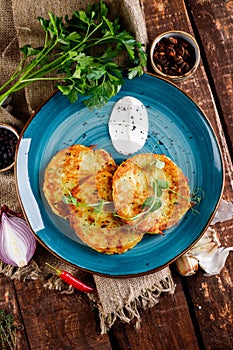 Close-up view of potato pancakes. Potato cake on a blue plate above a wooden table, with fresh parsley and sour cream