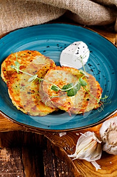 Close-up view of potato pancakes. Potato cake on a blue plate above a wooden table, with fresh parsley and sour cream