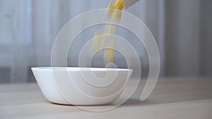 Close-up view of pouring corn flakes in a white plate.