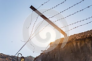 Close-up view prison or border concrete wethered fence broken old rusty barbed wire chain security barrier silhouette