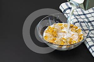 Close up view of process of pouring milk into glass bowl with cornflakes. Healthy eating concept.