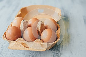 Close up view of raw chicken eggs in egg box on white wooden table.