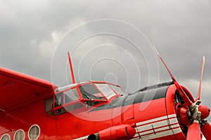 Close up view of red airplane biplane with piston engine and propeller on the cloudy sky background