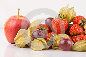 Close up view of red apple with orange physalis, purple grapes and red strawberries.