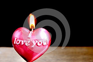 Close up view of red burning candle in the shape of heart on dark background.
