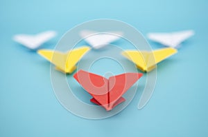 Close up view of red paper airplane origami leading yellow and white paper airplanes on blue cover background