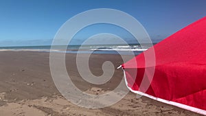 Close up view of a red umbrella swaying on a windy day at the beach.