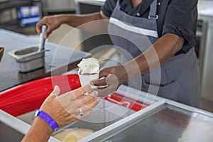 Close up view of a restaurant worker handing a cup of ice cream to a tourist.