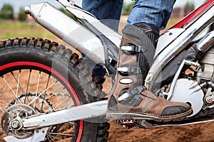 Close up view at rider`s motocross boot standing on peg of dirt motorcycle. Safety apparel for riding