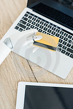 close-up view of robot holding credit card above laptop