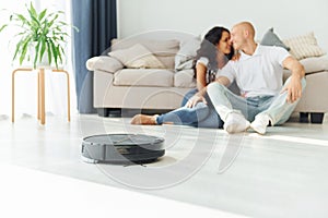 Close up view of robot vacuum cleaner. Cheerful couple is together indoors