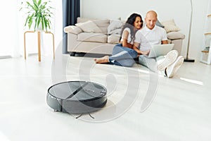 Close up view of robot vacuum cleaner. Cheerful couple is together indoors