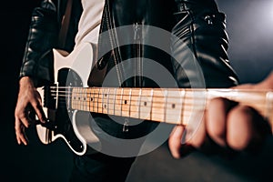 Close-up view of rock musician mans hands masterfully playing electric guitar. Fingers tapping strings in smoky