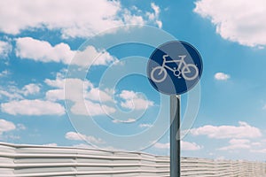 Close-up view of round blue and white bicycle lane sign against a fence and blue sky with clouds. Outdoor sign. Traffic Laws.