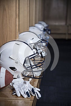 Close up view of a row of American football helmets sitting in a locker room before an football game. Gloves and a football also s photo