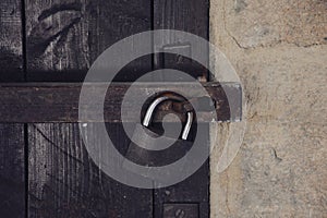 Close up view of a rusty padlock on weathered vintage wooden door with an old castle stone wall.