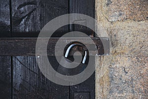 Close up view of a rusty padlock on weathered vintage wooden door with an old castle stone wall.