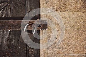 Close up view of a rusty padlock on weathered vintage wooden door with an old castle stone wall.