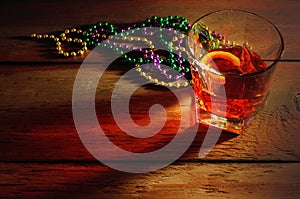 Close-up view of sazerac cocktail with a lemon peel in glass on wooden table with side lighting and warm tones.