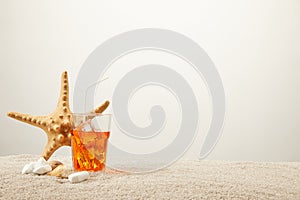 close up view of sea star, refreshing cocktail with straw and seashells on sand on grey background