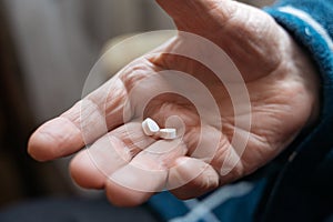 Close up view of senior male hand holding two pills while feeling bad and taking treatment. Focus on his hand. Wrinkled