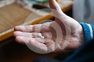 Close up view of senior male hand holding two pills while feeling bad and taking treatment. Focus on his hand. Wrinkled