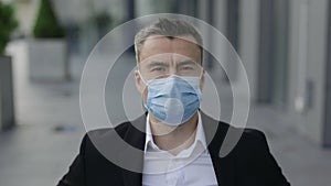 Close up view of serious male ceo executive wearing medical protective mask while looking to camera. Portrait of man in