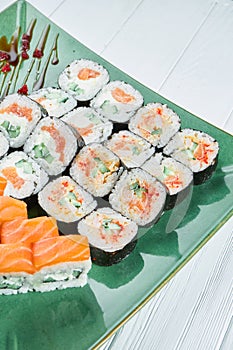 Close up view on set of assorted roll and sushi on green plate isolated on white wooden background. Sushi with salmon, eel.