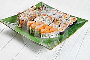 Close up view on set of assorted roll and sushi on green plate isolated on white wooden background. Sushi with salmon, eel.