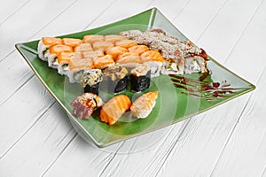 Close up view on set of assorted roll and sushi on green plate isolated on white wooden background. Sushi with salmon, eel.