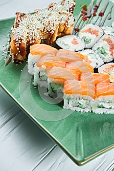 Close up view on set of assorted roll and sushi on green plate isolated on white wooden background. Sushi with salmon, eel.