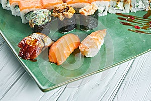 Close up view on set of assorted sushi on green plate isolated on white wooden background. Sushi with salmon, eel. shrimp japanese