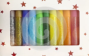 Close-up view of a set of small, colorful, glitter glue tubes arranged in a row within a white cardboard box photo