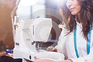 Close-up view of sewing machine and young female tailor working on it while sitting in a workshop