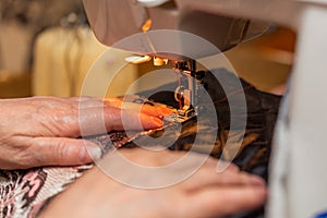 A close-up view of sewing process, hand of old woman using sewing machine, selective focus technique